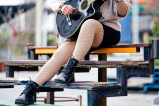 eine Frau spielt Gitarre und trägt flachgestrickte Kompressionsstrümpfe Farbe Cashmere mit Ornamenten
