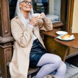 Frau sitzt mit einem Kaffee auf der Bank und trägt neue Kompressionsstrümpfe in Grau von medi