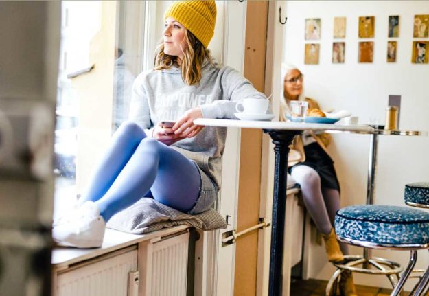 junge Frau sitzt auf einer Fensterbank und trägt Kompressionsstrümpfe in neuem Jeansblau