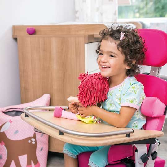 kleines Mädchen sitzt lachend in einer pinken Sitzhilfe