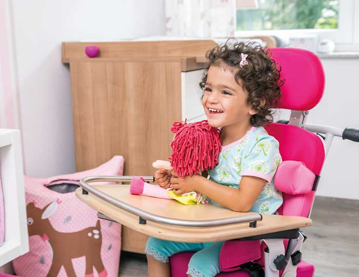 kleines Mädchen sitzt lachend in einer pinken Sitzhilfe