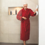 Frau im roten Bademantel hält sich an einem Duschgriff fest