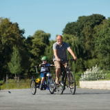 Erwachsener hat ein kleines Kind mit einer Tandemkupplung an sein Fahrrad angehängt