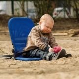 Kind sitzt sicher im Sand in einer Duschliege