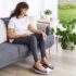 Frau sitzt auf Sofa und massiert ihre müden Beine elektronisch mit Revitive Medic
